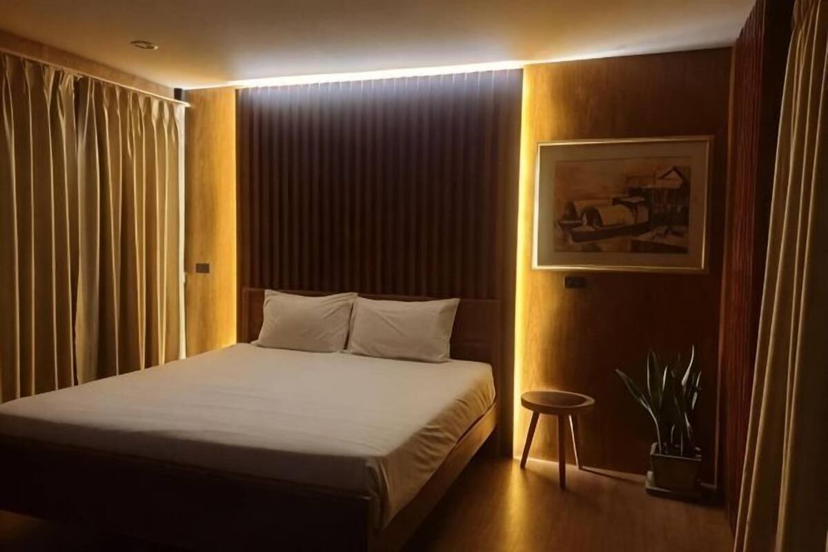 Een hotelkamer met een bed, een klein tafeltje, een potplant en een schilderij aan de muur.