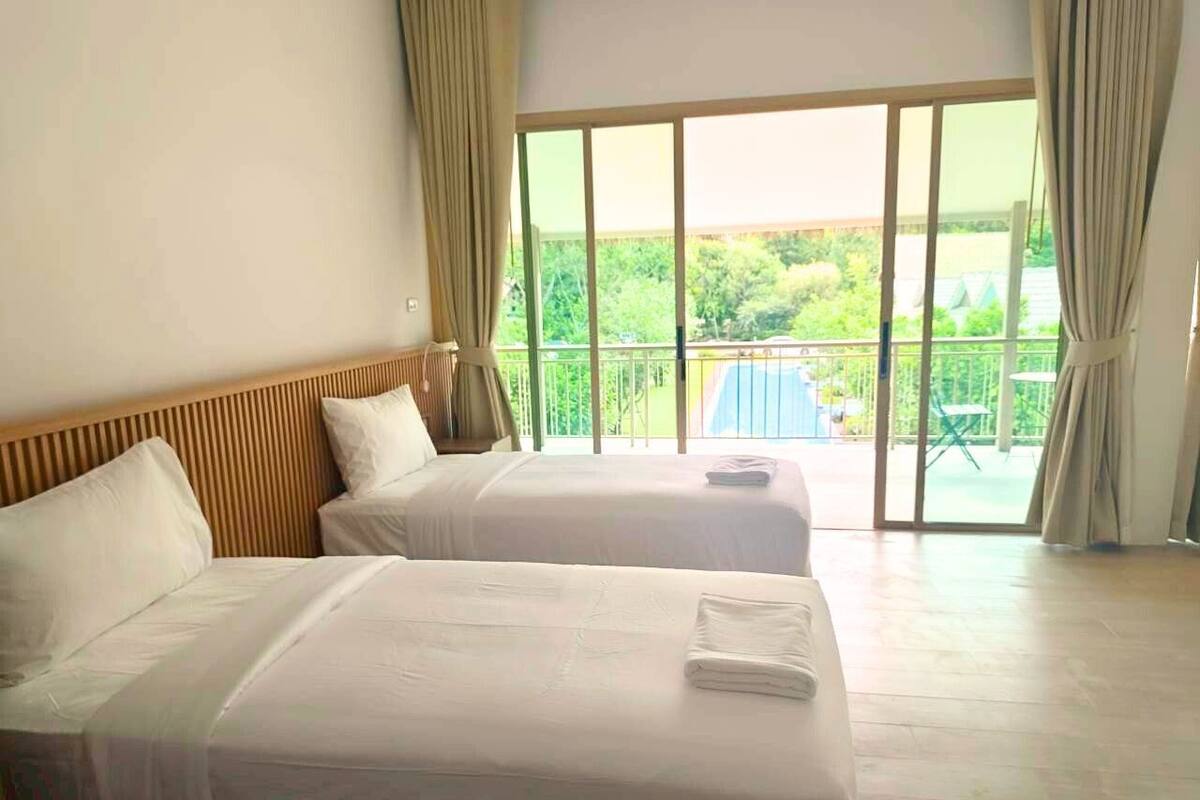 Een hotelkamer met twee bedden, een balkon met uitzicht op groen en een schuifdeur van glas.