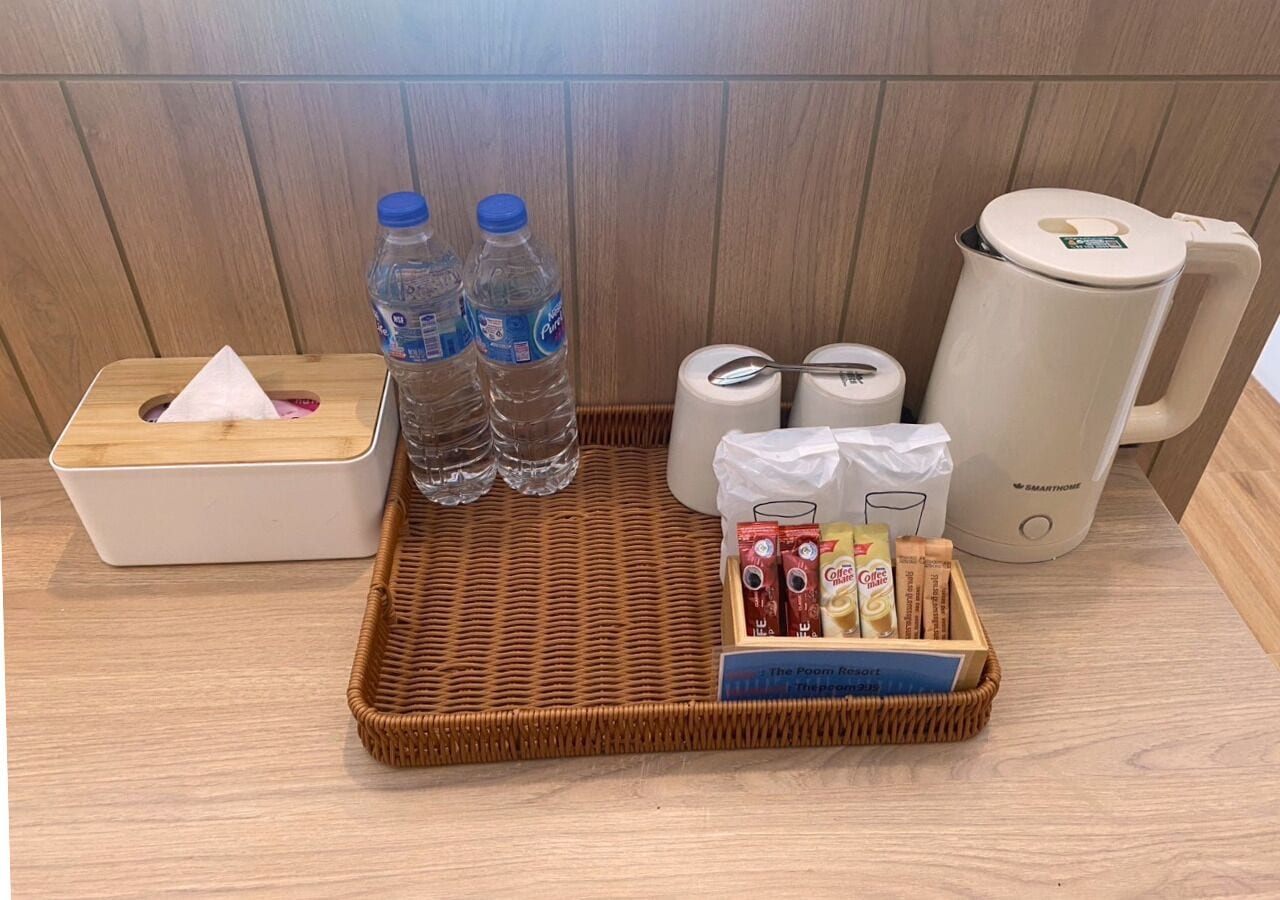 Comodidades do quarto de hotel, incluindo uma bandeja de vime com água engarrafada, lenços de papel, uma cafeteira e uma cesta de lanches.