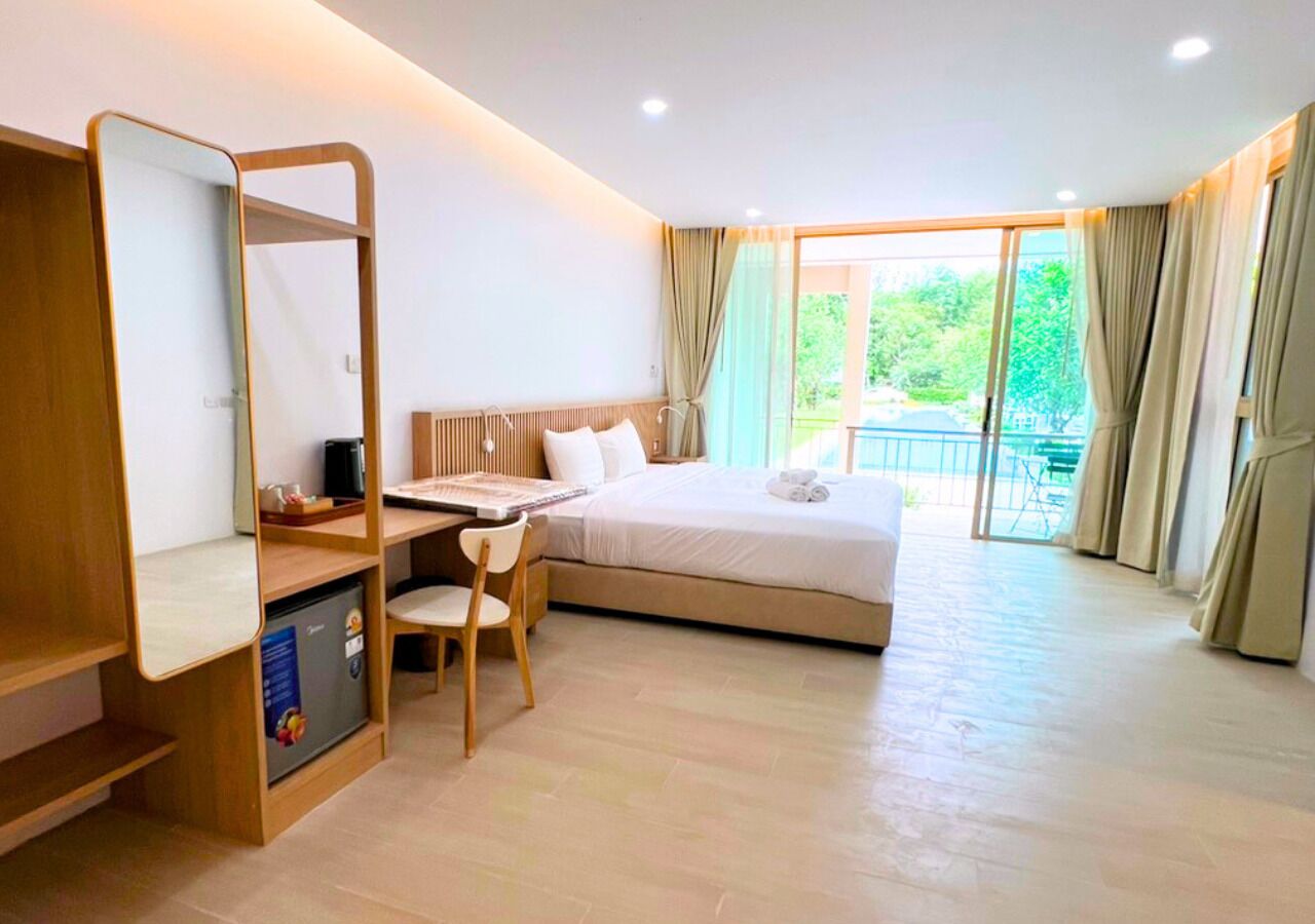 Une chambre d’hôtel comprenant un lit, un bureau avec une chaise, un petit réfrigérateur et une grande fenêtre avec des rideaux.