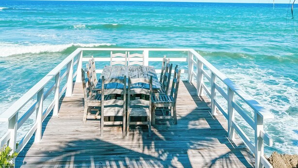 A wooden pier with white railings leading to the ocean, with a table and chairs set up for dining. - 4 Bedroom Luxury Villa Peninsula Esmeralda Luxury Hotel & Villas (Cofresi)