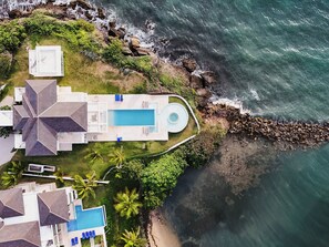 Vue aérienne d’une propriété située sur la côte, avec une piscine, plusieurs bâtiments et une côte rocheuse.