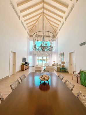 A spacious room with a high ceiling, a chandelier, a long dining table, and a view of a pool. - 4 Bedroom Luxury Villa Peninsula Esmeralda Luxury Hotel & Villas (Cofresi)