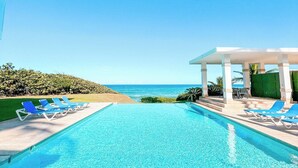 A clear blue pool with lounge chairs, a covered seating area, and a view of the ocean. - 4 Bedroom Luxury Villa Peninsula Esmeralda Luxury Hotel & Villas (Cofresi)