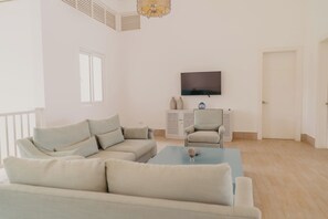 Ein Wohnzimmer mit einem Ecksofa, einem kleinen Tisch, einem Fernseher und einem Schrank.