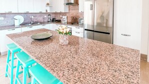 A modern kitchen with a large granite island, stainless steel appliances, and teal bar stools. - 4 Bedroom Luxury Villa Peninsula Esmeralda Luxury Hotel & Villas (Cofresi)