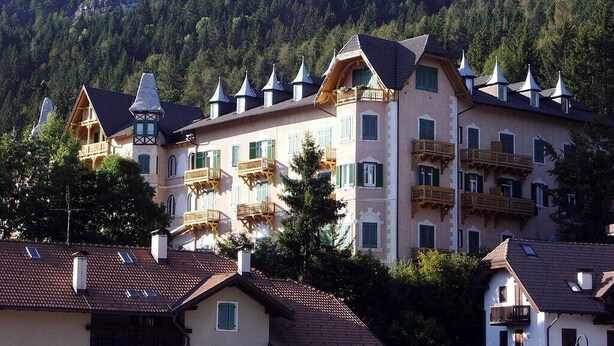 Un immeuble à plusieurs étages doté de balcons, avec une chaîne de montagnes en arrière-plan et un style architectural traditionnel.