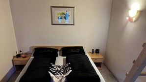 Un lit bien fait, agrémenté d’oreillers noirs, une œuvre d’art encadrée au-dessus, et une table de chevet avec un téléphone et une petite lampe.