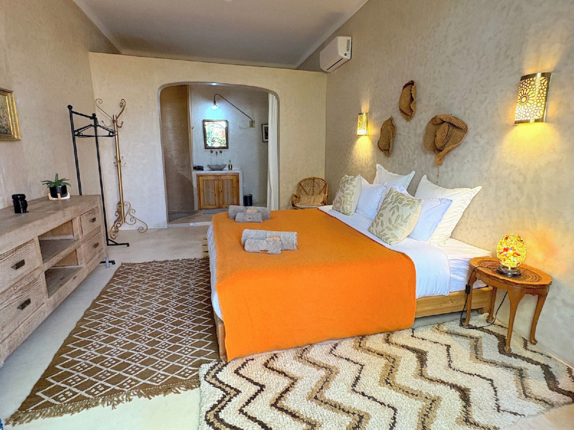 A hotel room with a bed, a wooden dresser, a patterned rug, and a nightstand with a lamp.