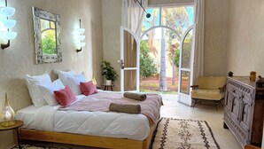 A bedroom with a large bed, a wooden nightstand, a lamp, a mirror, a dresser, and a view of the outdoors. - Palais Bohemia (Zouhria)