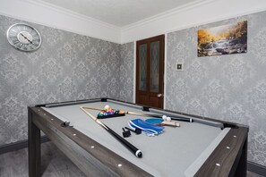 Ein Billardtisch mit Billardkugeln und Spielstöcken, eine Uhr und eine Tür in einem Raum mit gestreiftem Wandpapier.