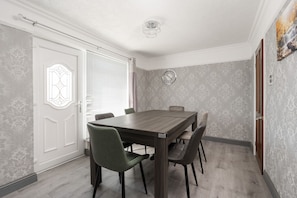 Comedor con mesa de madera y cuatro sillas, un reloj en la pared y un papel tapiz estampado.