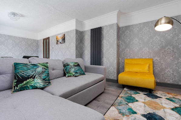 Una sala de estar moderna con un sofá seccional gris, un sillón amarillo y una alfombra estampada.