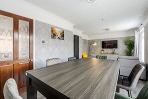 Ein modernes Wohnzimmer mit einem großen Esstisch aus Holz, einer Couch und einem an der Wand montierten Fernseher.