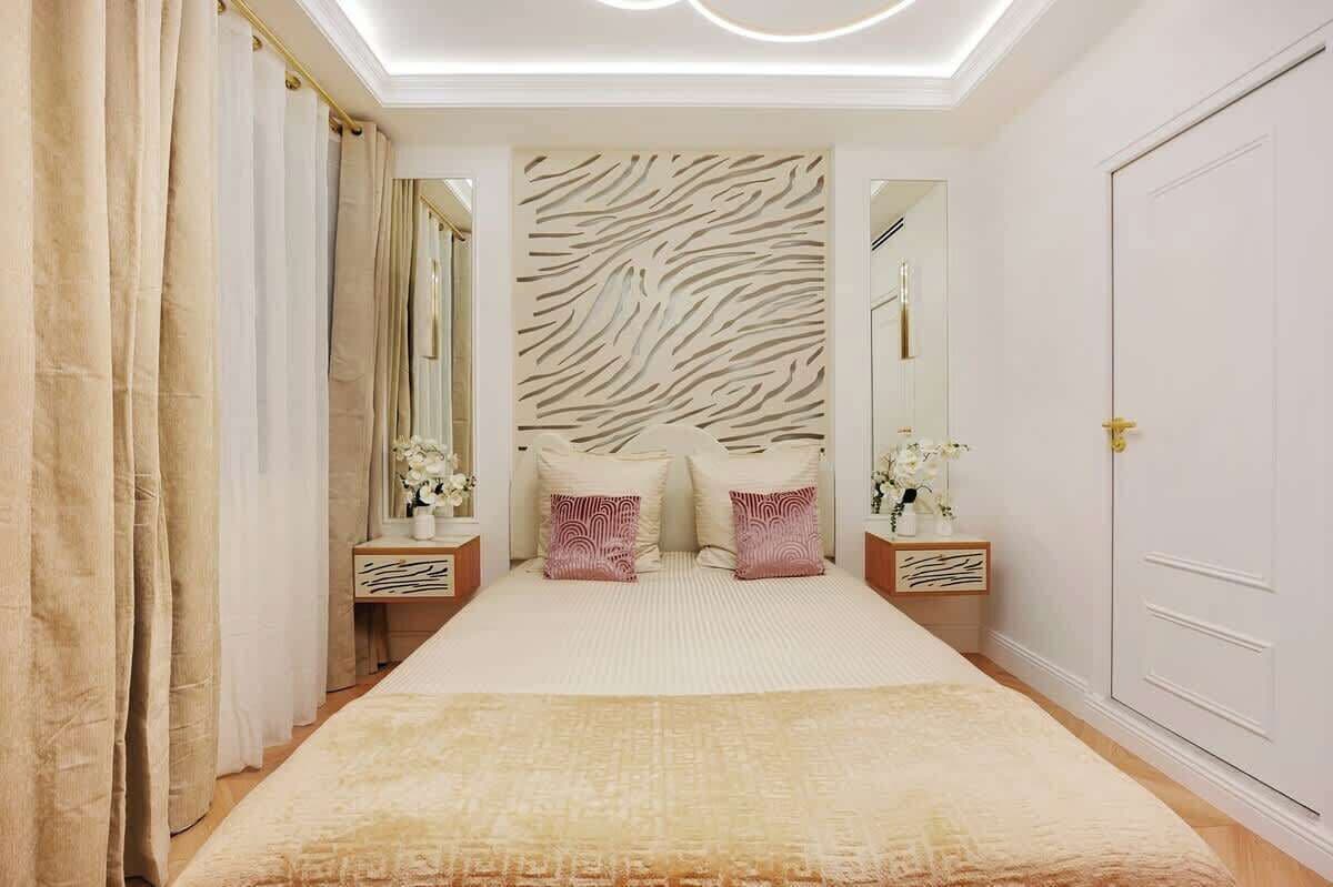 Een slaapkamer met een hoofdeinde met zebraprint, een groot bed met een beige en witte dekbedovertrek, twee nachtkastjes met lampen, en een deur aan de rechterkant.