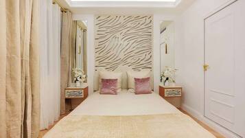 Een slaapkamer met een hoofdeinde met zebraprint, een groot bed met een beige en witte dekbedovertrek, twee nachtkastjes met lampen, en een deur aan de rechterkant.