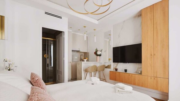 Ein modernes Hotelzimmer mit einem großen Bett, einem Holzschrank, einem Fernseher und einer Küchenzeile im Hintergrund.