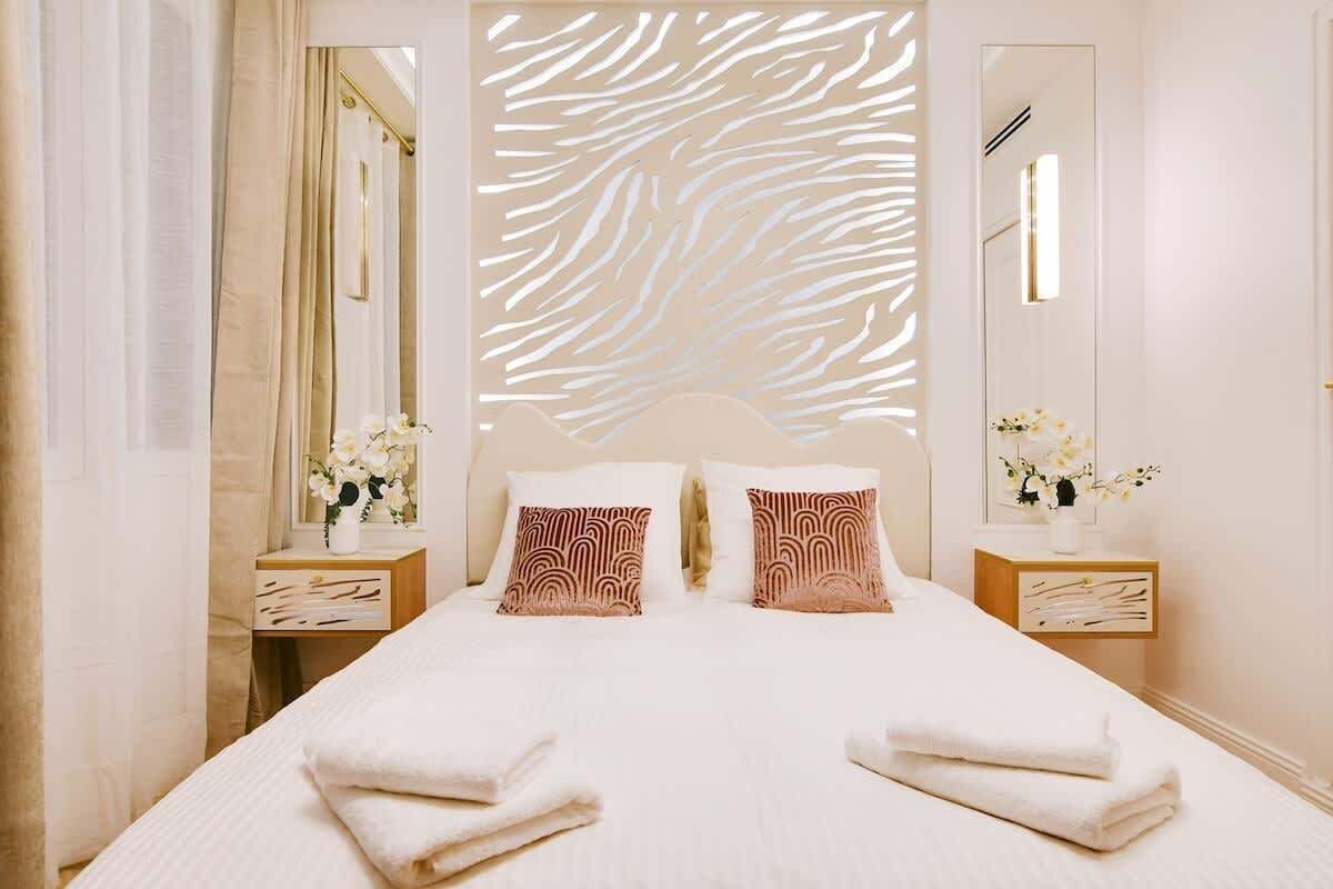 Une chambre d’hôtel avec un grand lit, deux tables de chevet, un miroir et un panneau décoratif au mur.