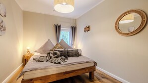 Een slaapkamer met een houten bed, een bedlampje, een spiegel en een raam met gordijnen.