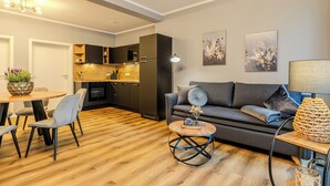 Een moderne woonkamer met een grijze bank, een ronde salontafel, en een eethoek met een houten tafel en stoelen.