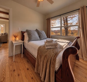 A bedroom with a wooden bed, a nightstand with a candle, and a window with curtains.