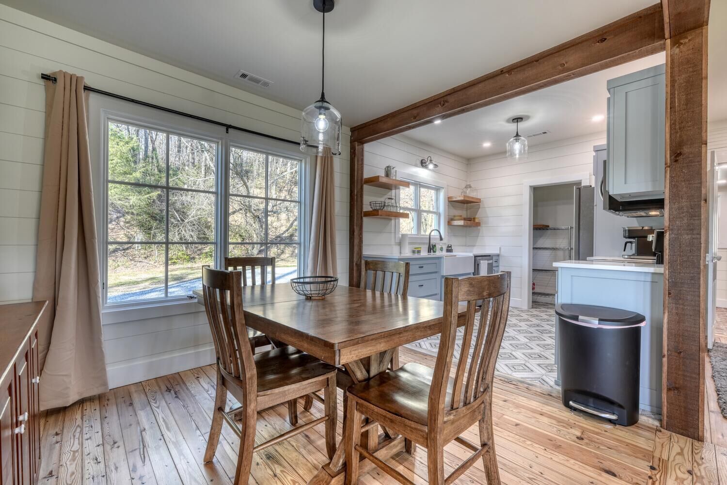 Un coin repas avec une table et des chaises en bois, une fenêtre avec des rideaux et une vue sur l’extérieur.