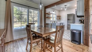 Un comedor con una mesa y sillas de madera, una ventana con cortinas y vistas al exterior.