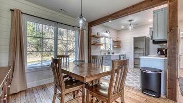 Un coin repas avec une table et des chaises en bois, une fenêtre avec des rideaux et une vue sur l’extérieur.