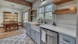 Una cocina moderna con vigas de madera, un comedor con mesa y sillas, y vistas a árboles a través de amplios ventanales.