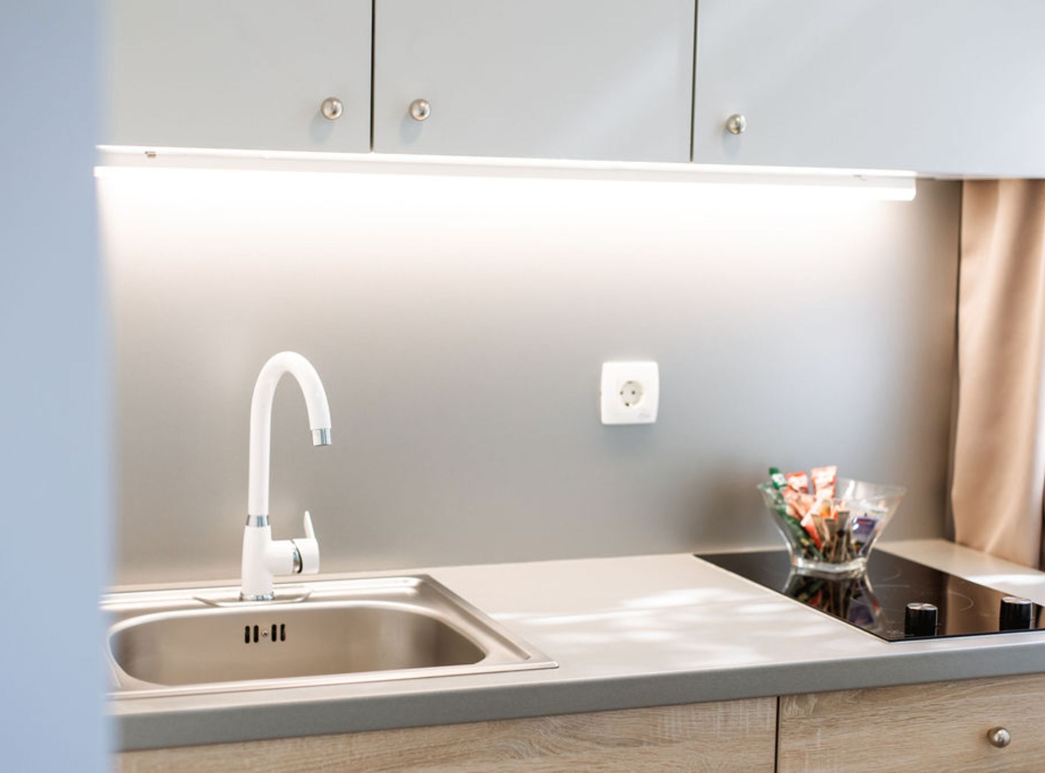 A modern kitchen with a stainless steel sink, a white faucet, and a lighted countertop.