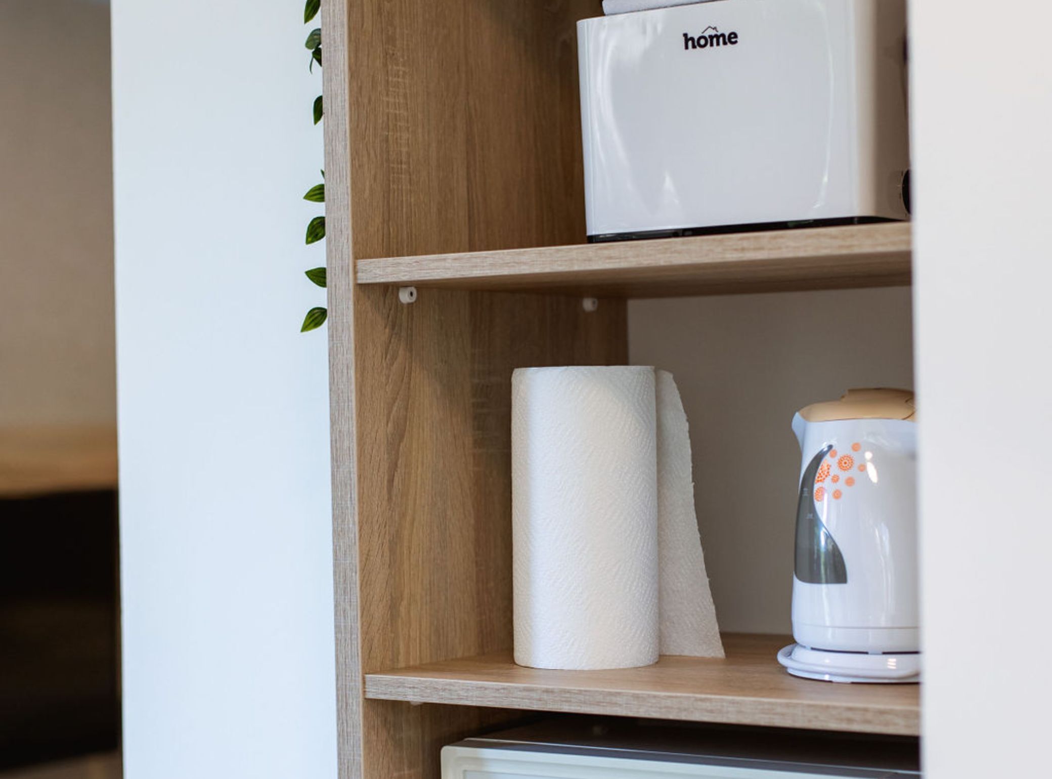 A wooden shelf with a white box labeled "home" and a white kettle on the right.