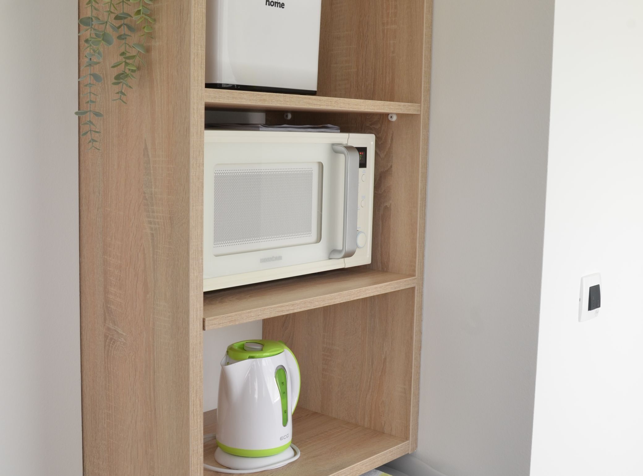 A wooden shelf unit with a microwave and a kettle.