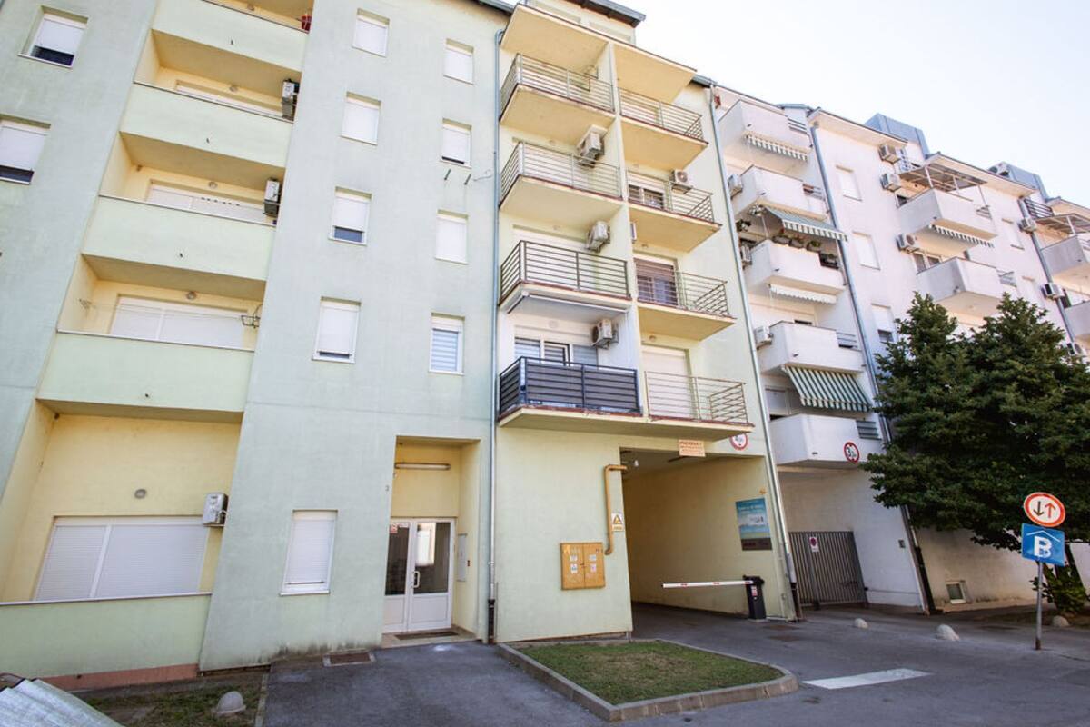 A multi-story residential building with balconies, a gated entrance, and a parking sign.