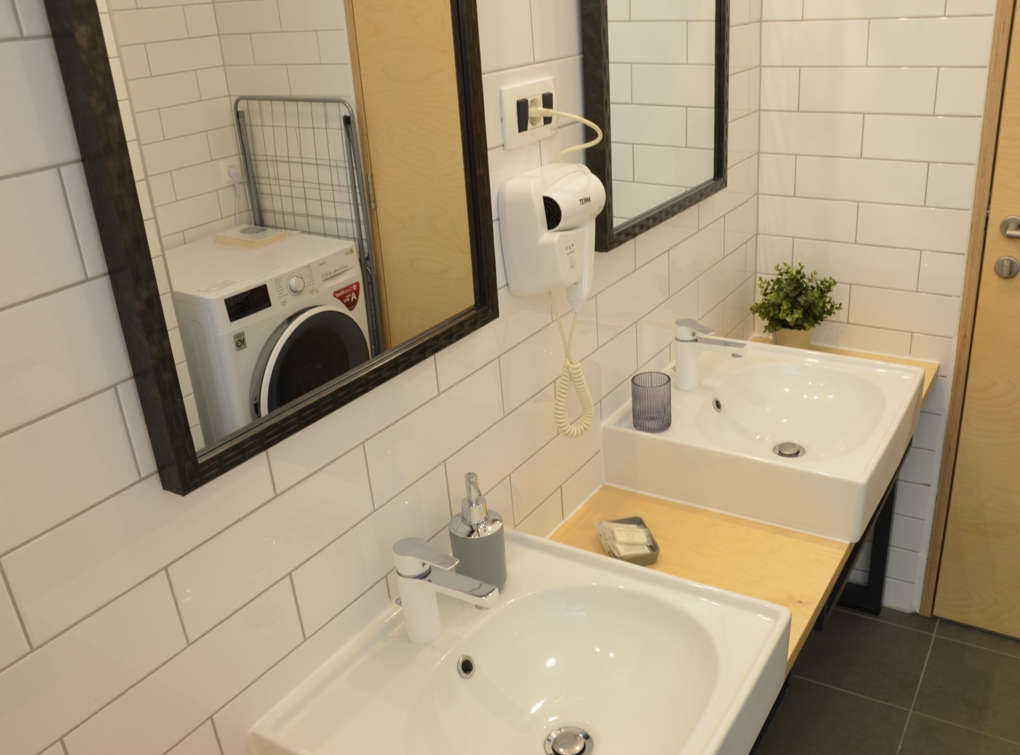 A modern bathroom with two sinks, a mirror, a washing machine, and a telephone.