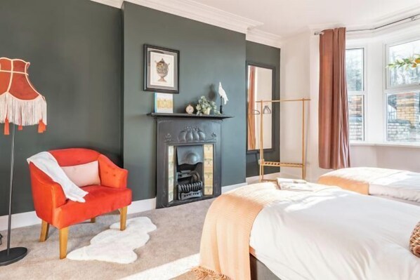 A hotel room with a fireplace, a red armchair, two beds, and a large window. - 4 Bedroom Home w/ Free Parking - Tŷ Hapus Newport (Beechwood)