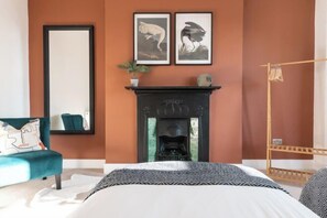 A bedroom with a bed, a fireplace, a mirror, and a wardrobe. - 4 Bedroom Home w/ Free Parking - Tŷ Hapus Newport (Beechwood)