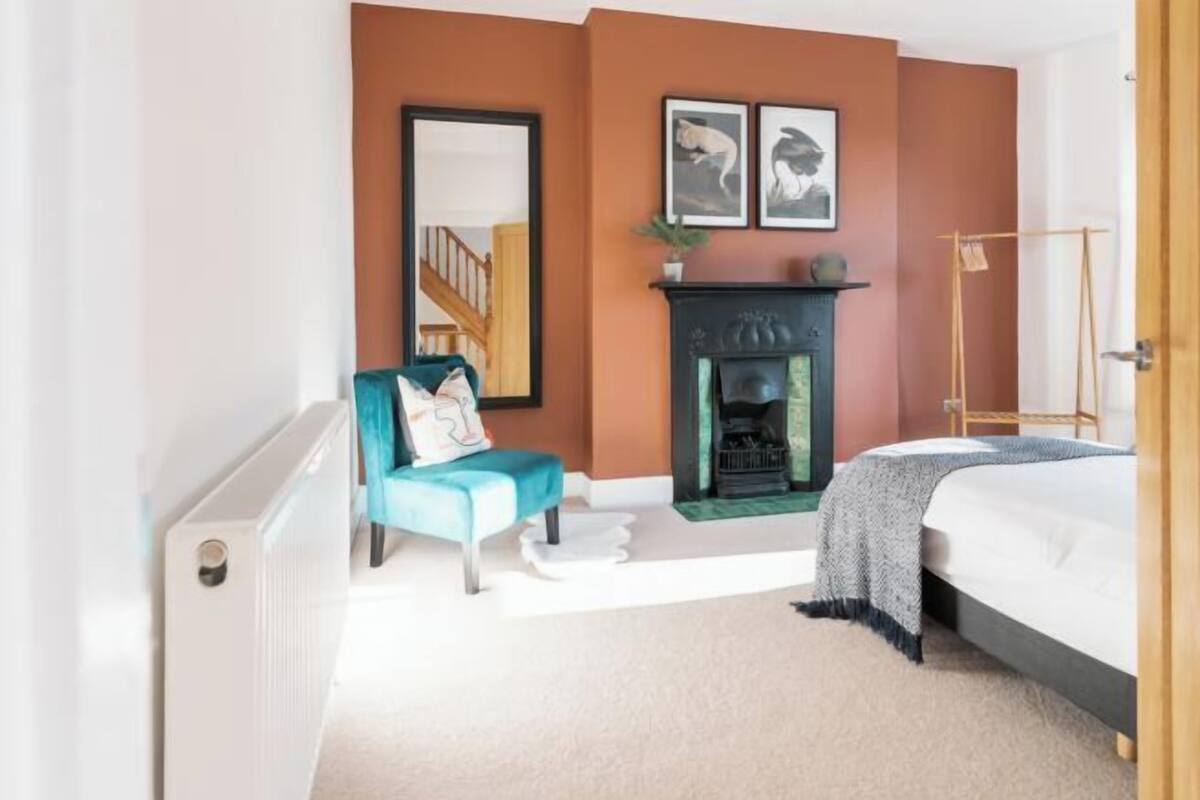 A bedroom with a fireplace, a bed, a chair, and a mirror.