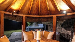 Ein Holzpavillon im Freien mit Tisch, Stühlen, einer Whirlwanne und einer Backsteinmauer.
