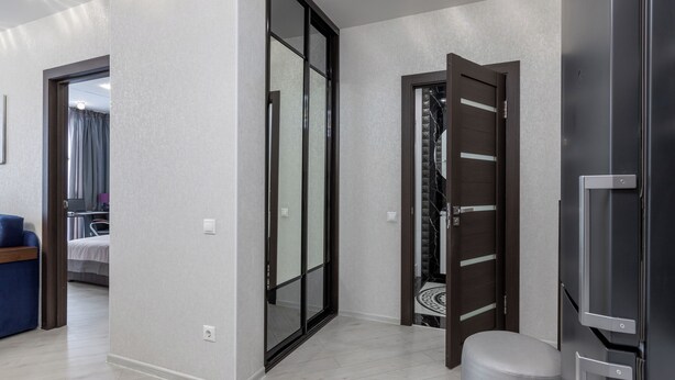 Un intérieur moderne avec un couloir menant à une chambre, une porte en bois foncé et un meuble télé intégré.