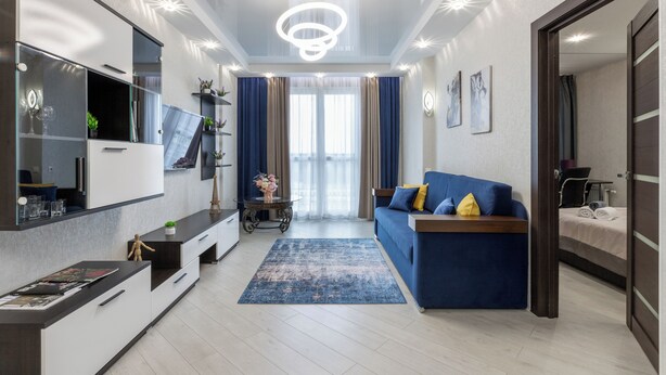 A modern living room with a blue sofa, a flat-screen TV, a coffee table, and a large mirror. - Modern apartments  near Dana Mall (Minsk)