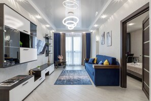 Ein modernes Wohnzimmer mit einem blauen Sofa, einem Flachbildfernseher, einem Couchtisch und einem großen Spiegel.