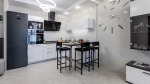 A modern kitchen with a built-in oven, a black refrigerator, and a dining area with two black chairs. - Modern apartments  near Dana Mall (Minsk)