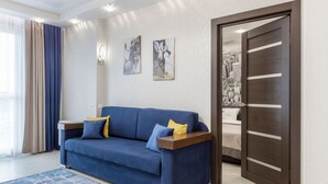 A modern living room with a blue sofa, a wooden side table, and a cityscape artwork on the wall. - Modern apartments  near Dana Mall (Minsk)
