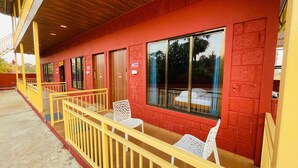 A row of rooms with large windows, a wooden ceiling, and a yellow railing. - Amantran Farms and Resort (Karjat)
