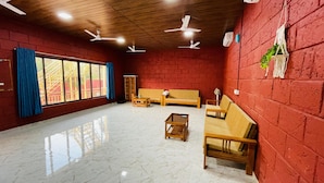 A spacious room with a red brick wall, a large window with blue curtains, and multiple ceiling fans. - Amantran Farms and Resort (Karjat)