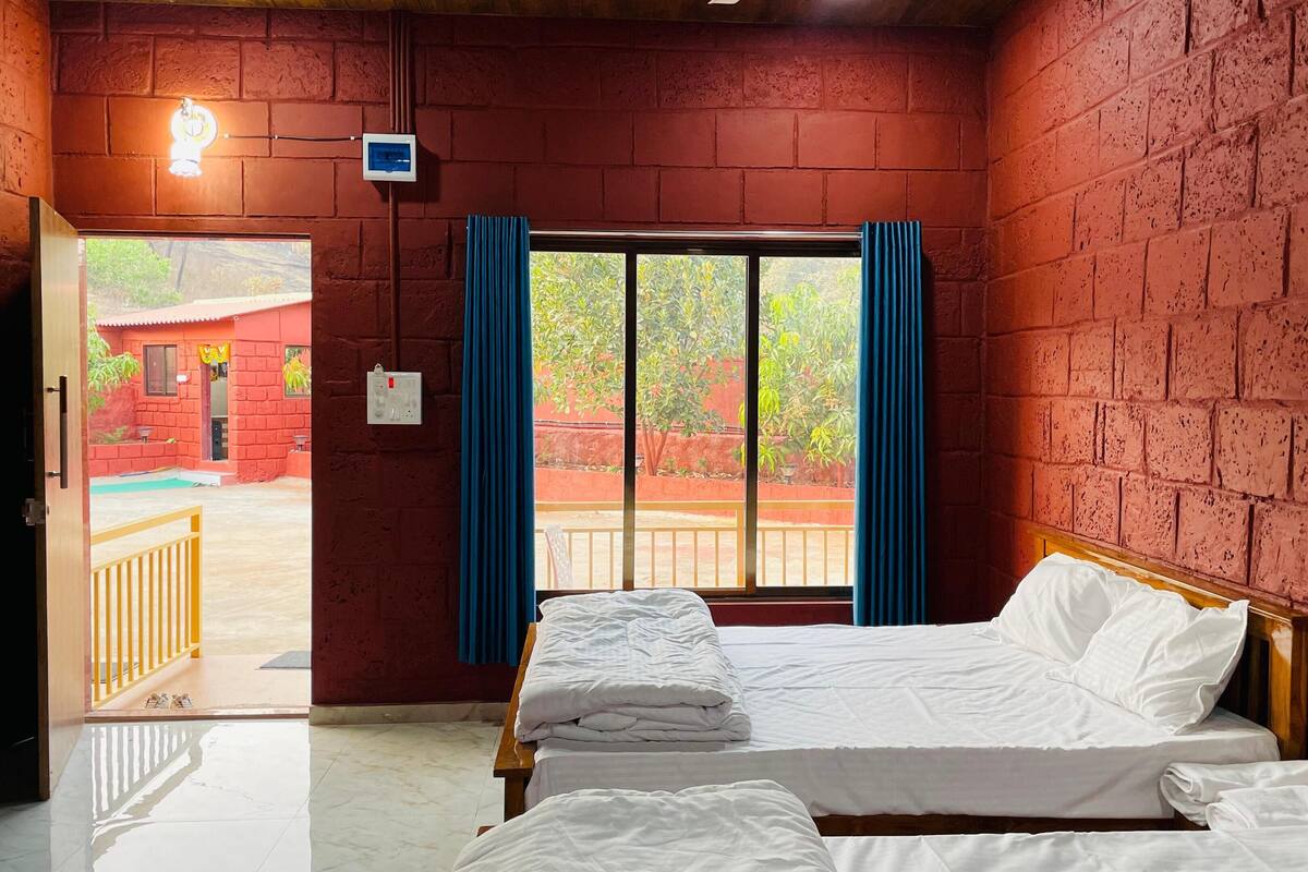 A hotel room with a bed, a window with curtains, a view of the outside, and a brick wall.