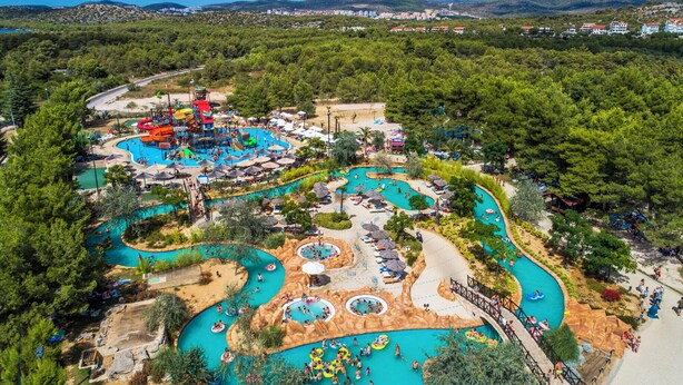 An aerial view of a water park with multiple pools, slides, and a winding road.