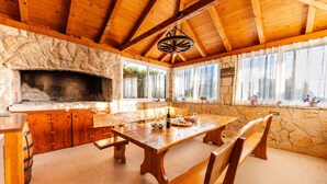 A rustic interior with a stone fireplace, wooden dining table, benches, and large windows.