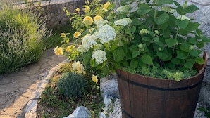 A garden with a wooden barrel planter filled with flowers, a stone wall, and a stone building in the background.