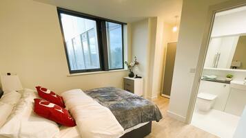 A bedroom with a bed, a window, a bedside table, and a bathroom with a mirror and sink.
